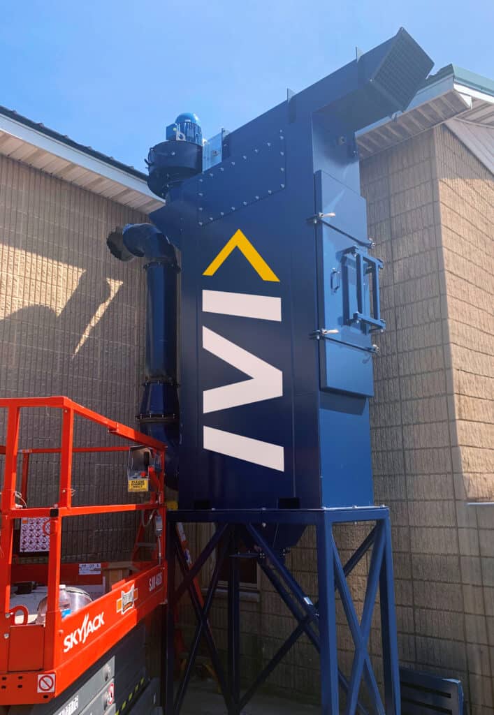 Blue cartridge dust collector for foundry blast machine on outside of industrial building